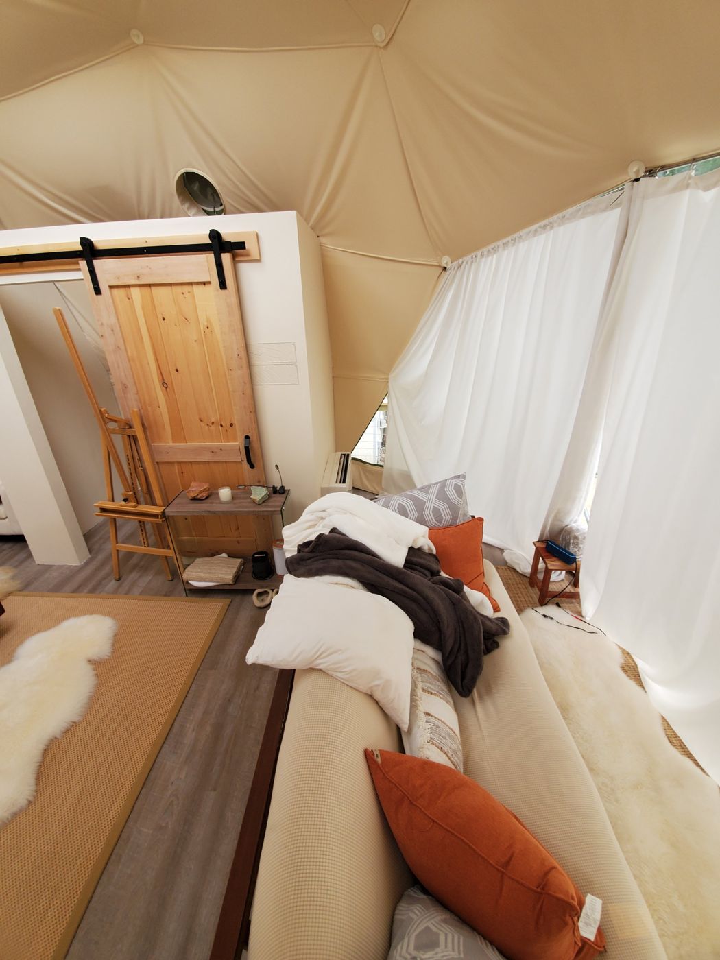 Interior of the glamping dome with sofa, sheepskins and a barn door, with the heat pump console tucked out of the way