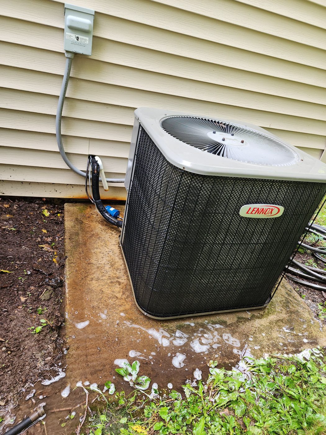 Lennox central air conditioner condenser on a concrete pad, with cleaning foam rinsing off the coil