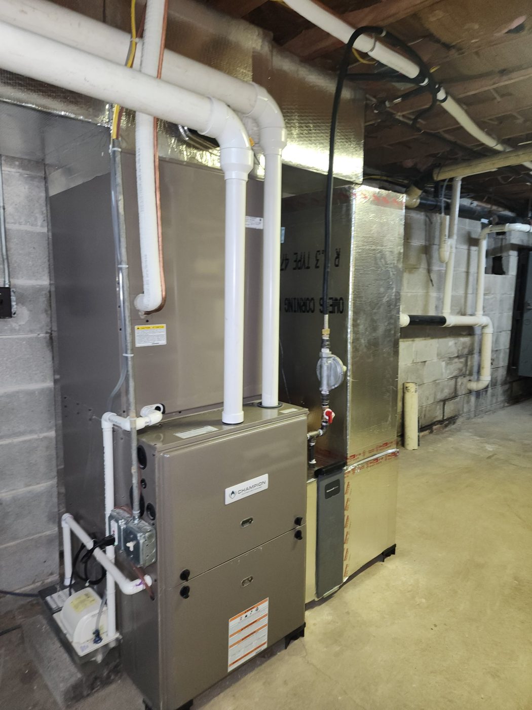 Newly installed Champion high-efficiency gas furnace in a basement, with white PVC intake and exhaust pipes, foil-wrapped supply plenum and a condensate pump