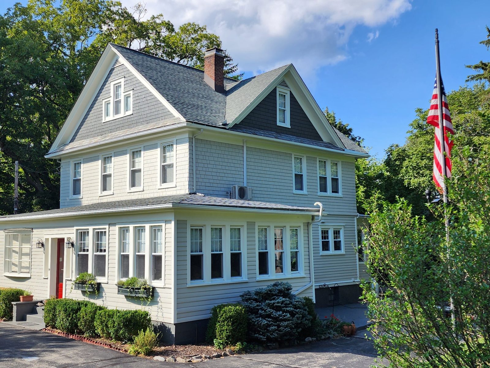 Ductless mini-split outdoor unit mounted on the side of a two-story shingle-style home in summer