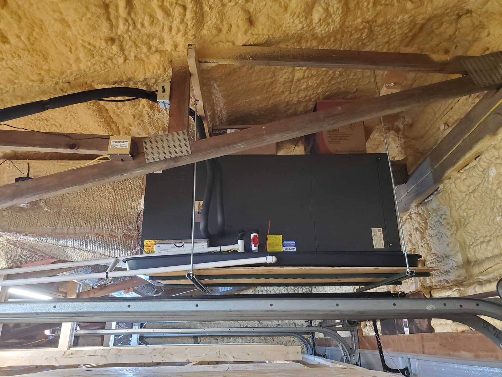 Mitsubishi Electric ducted air handler suspended on threaded rod and strut in a spray-foam insulated attic, with drain pan, condensate line and UV light