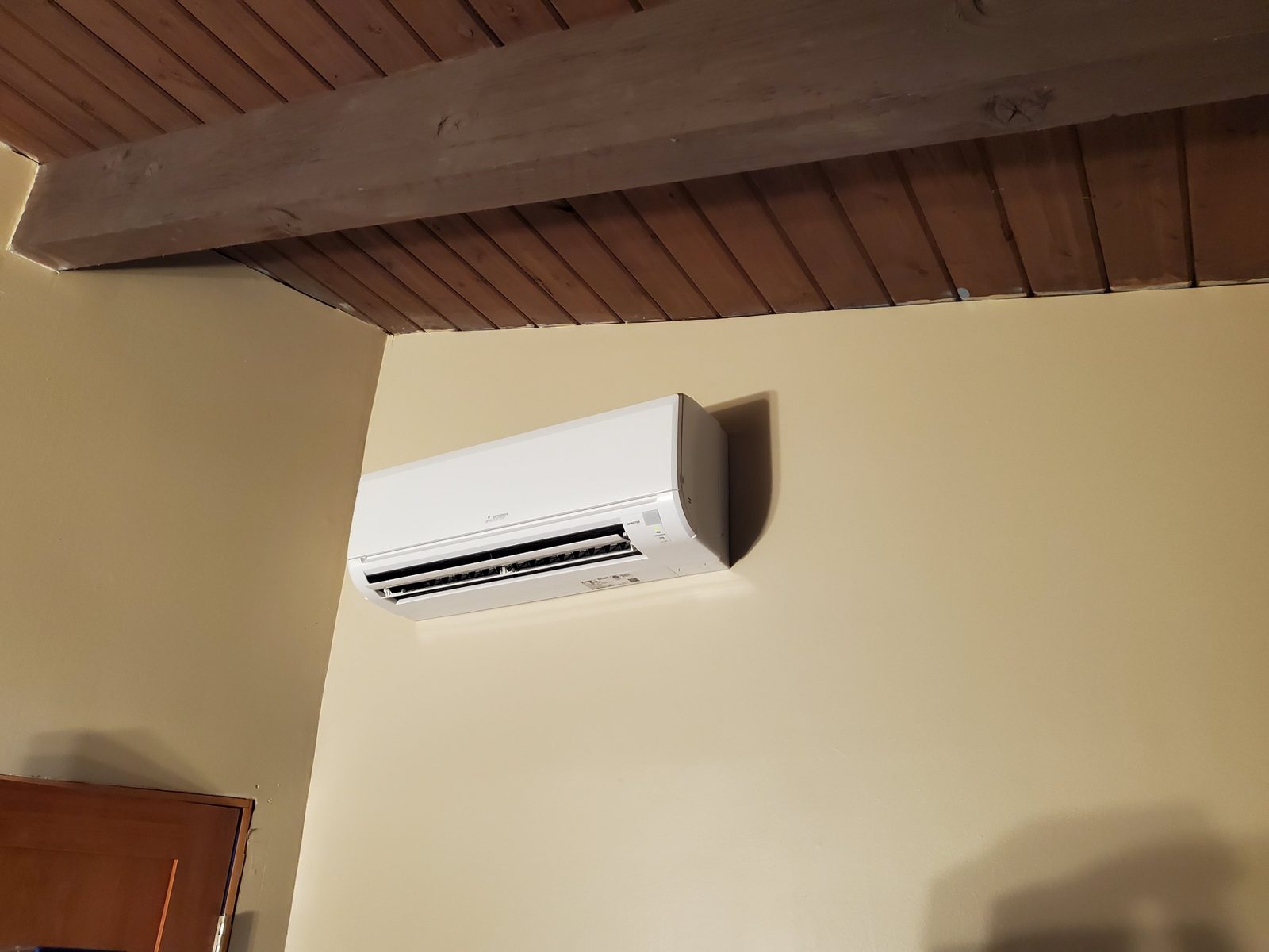 Mitsubishi Electric ductless wall unit mounted high on a cream wall beneath a wood plank ceiling and exposed beam