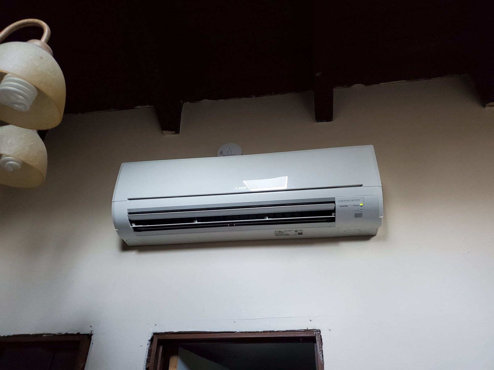 Mitsubishi Electric wide-airflow ductless wall unit mounted above a doorway, running with its indicator light on