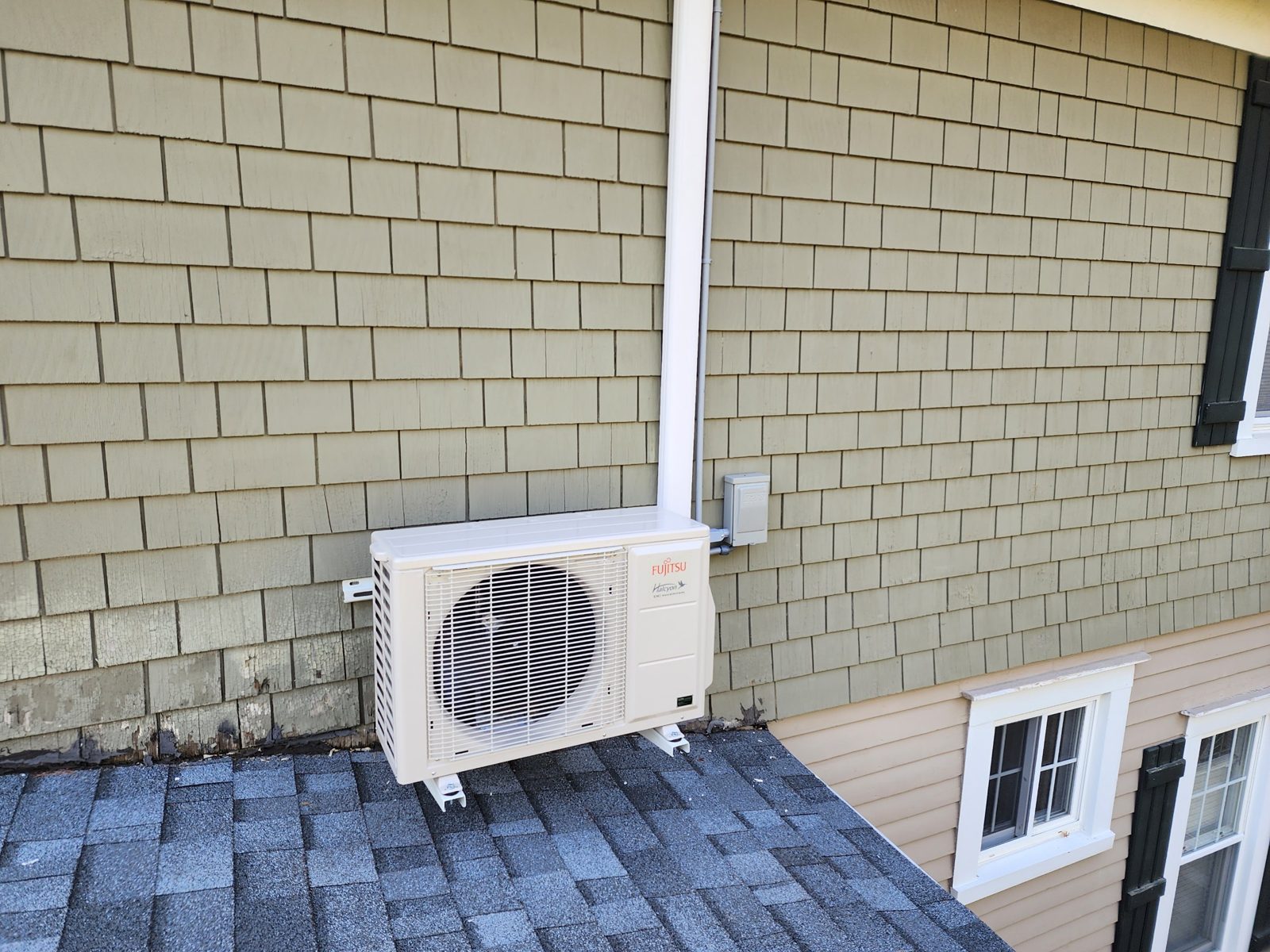 Fujitsu Halcyon heat pump outdoor unit mounted on brackets on a low roof, with the line set and disconnect neatly run up the wall